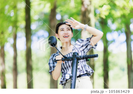 陽射しを浴びながら電動キックボードに乗る若い女性 陽射しを浴びながら電動キックボードに乗る若い女性 105863429