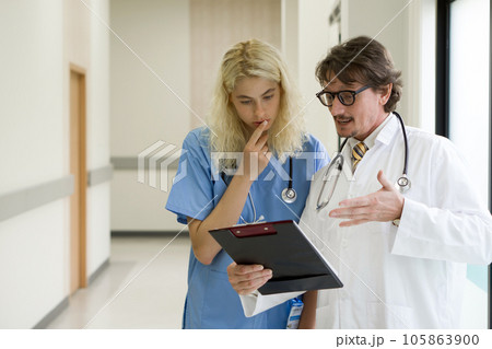 Two medical professionals engaging in a discussion within sanitized hospital corridors Two medical professionals engaging in a discussion within sanitized hospital corridors 105863900