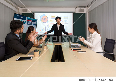 Enthusiastic diverse corporate team applauding in a meeting around a conference table, embodying collective decision making. 105864108