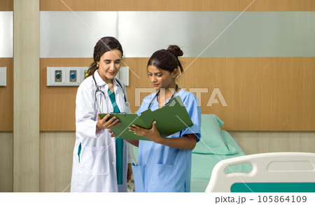 Two healthcare professionals clad in medical uniform amid their bustling environment, engaging in a discussion, backdrop of a hospital room. 105864109