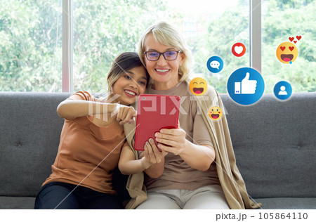 A candid image of two women comfortably seated on a couch, attentively browsing social media on a technology device with visible social media icons. 105864110