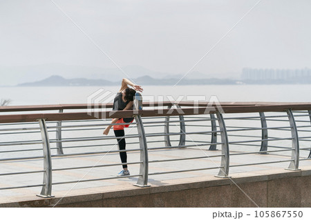 young asian woman in sportswear stretching legs outdoors in seaside park young asian woman in sportswear stretching legs outdoors in seaside park 105867550