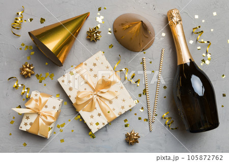 Flat lay composition of Champagne bottle gift box ribbons and confetti on colored background. Flat lay, top view holiday concept Flat lay composition of Champagne bottle gift box ribbons and confetti on colored background. Flat lay, top view holiday concept 105872762