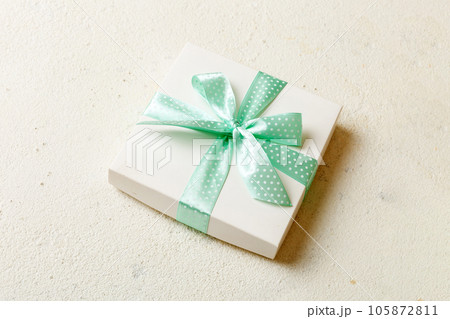 wrapped Christmas or other holiday handmade present in white paper with green ribbon on colored background. Present box, decoration of gift on colored table, top view with copy space 105872811