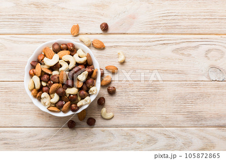 Assortment of nuts in wooden bowl on colored table. Cashew, hazelnuts, walnuts, almonds. Mix of nuts Top view with copy space 105872865