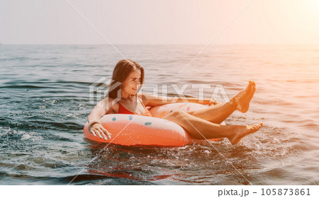 Woman summer sea. Happy woman swimming with inflatable donut on the beach in summer sunny day, surrounded by volcanic mountains. Summer vacation concept. Woman summer sea. Happy woman swimming with inflatable donut on the beach in summer sunny day, surrounded by volcanic mountains. Summer vacation concept. 105873861