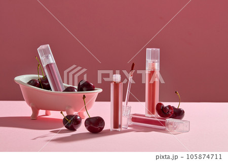 Several lipsticks are arranged with cherries and a bathtub over pink background. Cherries are a good source of vitamins A, B, C and E 105874711