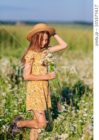 Portrait of girl in a yellow dress and straw hat on a chamomile field in summer Portrait of girl in a yellow dress and straw hat on a chamomile field in summer 105875617