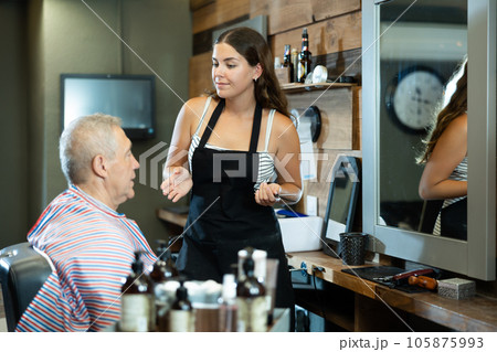 Young female barber discussing haircut with elderly client in barbershop 105875993