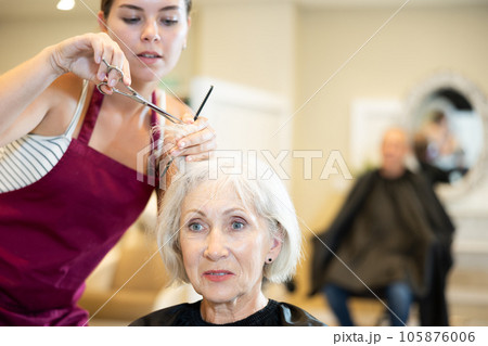 Young woman master completes creation of senior female clients image with help of scissors Young woman master completes creation of senior female clients image with help of scissors 105876006