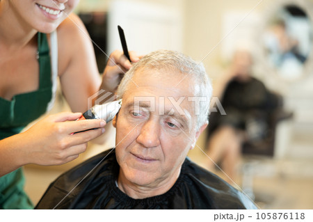Female hairdresser working hair clipper with older man Female hairdresser working hair clipper with older man 105876118