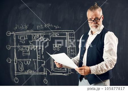 Stylish senior man, professional architect working with architectural design, making sketches on blackboard Stylish senior man, professional architect working with architectural design, making sketches on blackboard 105877817