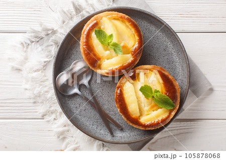 Ruddy baked Apple tart with custard decorated with mint close-up in a plate. Horizontal top view Ruddy baked Apple tart with custard decorated with mint close-up in a plate. Horizontal top view 105878068