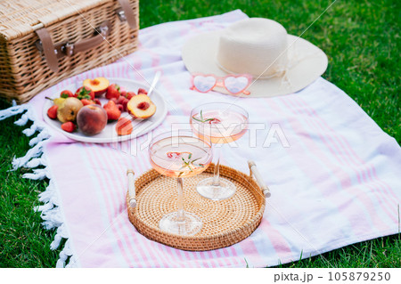 Pink drinks, cocktail with ice, raspberry, rosemary. Two glasses with martini, champagne, cider, lemonade on the blanket with fruit plate, picnic basket. Cozy summer picnic on nature. Selective focus 105879250