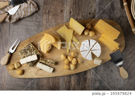 Cheese assorted on a wooden board, rustic style. Several varieties sliced cheeses: parmesan, tilsiter, halloumi with spices, camembert, smoked bocconcini, cheddar. Selective focus, close-up. 105879824