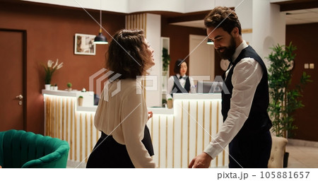 Businesswoman checking in luxury hotel, being helped by bellboy with luggage while receptionist checks booking details. Resort visitor in professional trip assisted by concierge personnel Businesswoman checking in luxury hotel, being helped by bellboy with luggage while receptionist checks booking details. Resort visitor in professional trip assisted by concierge personnel 105881657