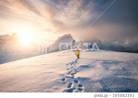 Mountaineer walking with footprint in snow storm and sunrise over snowy mountain in Senja Island Mountaineer walking with footprint in snow storm and sunrise over snowy mountain in Senja Island 105882381