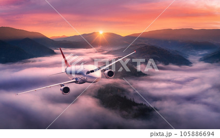 Airplane is flying above mountain peak in pink low clouds 105886694