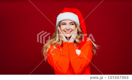 a cute beautiful woman in a Santa Claus hat on a red background. a cute beautiful woman in a Santa Claus hat on a red background. 105887868