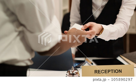 Close up of receptionist handing card key to elegant african american tourist during check in process. Business travelling guest ready to enjoy hotel stay after receiving room access 105890297