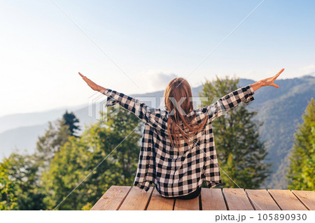 Back view of young girl sit on a terrace at a height in the mountains against the backdrop of fog and mountains 105890930