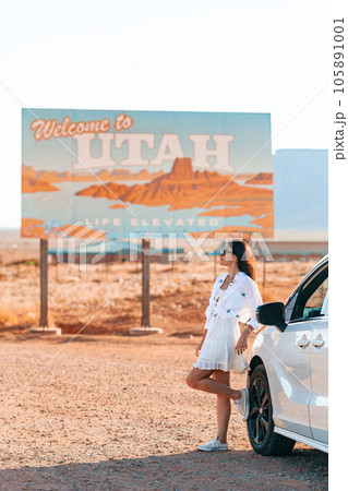Beautiful woman on her trip by the car. Welcome to Utah road sign. Large welcome sign greets travels in Monument Valley, Utah 105891001