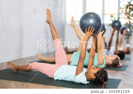 Portrait of childrens with pilates balls, pumping press during group class in fitness studio Portrait of childrens with pilates balls, pumping press during group class in fitness studio 105891284