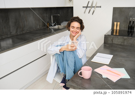 Beautiful girl with smartphone, sits at home, does homework, watches smth on mobile phone app 105891974