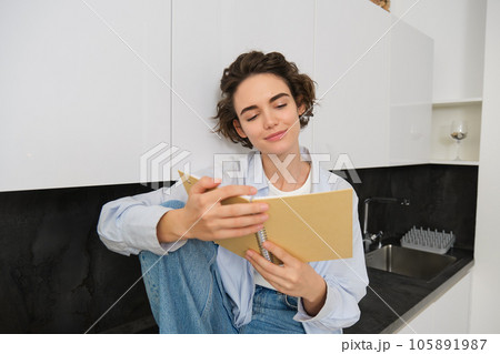 Portrait of smiling young woman reading journal, enjoys comfort at home, holding notebook, looking happy, relaxing indoors 105891987