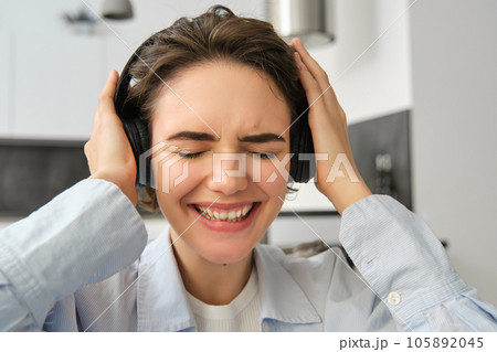 Close up portrait of woman, getting emotional from music, listening to song in wireless headphones, smiling and laughing Close up portrait of woman, getting emotional from music, listening to song in wireless headphones, smiling and laughing 105892045