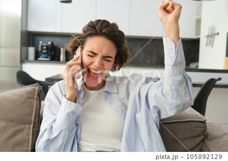Image of girl celebrating, holding smartphone and cheering from excitement, winning, receive great news on mobile phone 105892129
