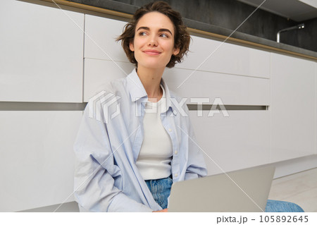 Young woman studying on floor. Girl with laptop works from home, types on computer, smiles and feels creative Young woman studying on floor. Girl with laptop works from home, types on computer, smiles and feels creative 105892645