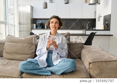 Portrait of smiling woman chats on smartphone app, sits at home on sofa and uses mobile phone application 105892787