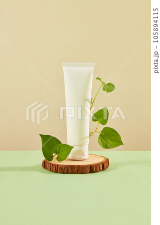 Front view of white plastic bottle unbranded with fresh fish mint leaves decorated on brown background. Mockup for advertising cosmetic extracted from fish mint with space for design packaging 105894115