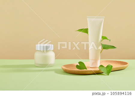 Mockup scene for advertising cosmetic extracted from fish mint. White plastic tube and jar unbranded decorated on wooden plates with fresh fish mint leaves on pastel background 105894116