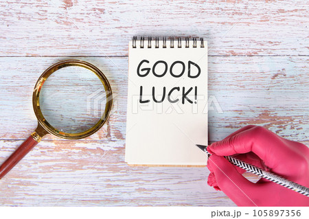 Good luck writing on a notebook lying on old boards next to a magnifying glass and a hand in a red medical glove with a pencil 105897356