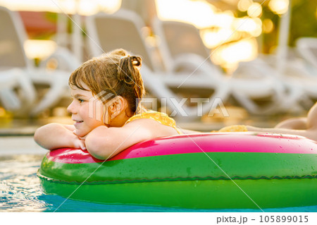 Happy little girl with inflatable toy ring float in swimming pool. Little preschool child learning to swim and dive in outdoor pool of hotel resort. Healthy sport activity and fun for children. 105899015