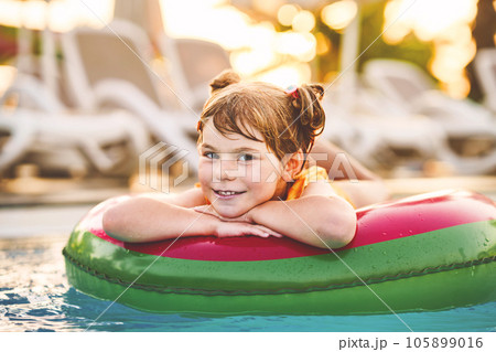 Happy little girl with inflatable toy ring float in swimming pool. Little preschool child learning to swim and dive in outdoor pool of hotel resort. Healthy sport activity and fun for children. Happy little girl with inflatable toy ring float in swimming pool. Little preschool child learning to swim and dive in outdoor pool of hotel resort. Healthy sport activity and fun for children. 105899016