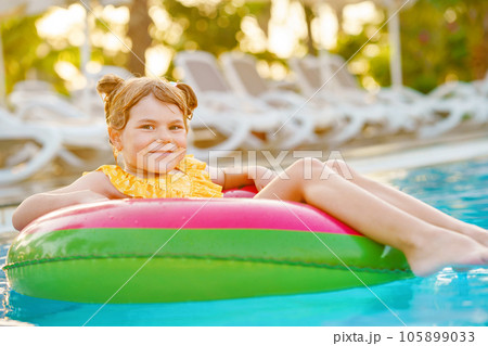 Happy little girl with inflatable toy ring float in swimming pool. Little preschool child learning to swim and dive in outdoor pool of hotel resort. Healthy sport activity and fun for children. Happy little girl with inflatable toy ring float in swimming pool. Little preschool child learning to swim and dive in outdoor pool of hotel resort. Healthy sport activity and fun for children. 105899033