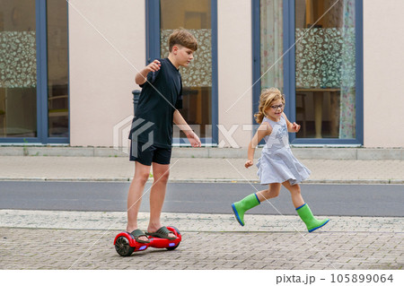 Little toddler girl running. School kid boy on hover board . Two happy children having fun with modern move gadgets, outdoor activity. Happiness, childhood. Excercise for kids. 105899064