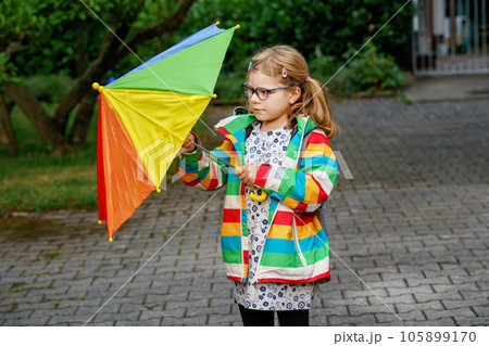 Little girl on way to elementary school or kindergarden. Preschool Child with colorful rainbow umbrella and waterproof jacket with school bag. Kid walking in autumn shower. Outdoor fun by any weather Little girl on way to elementary school or kindergarden. Preschool Child with colorful rainbow umbrella and waterproof jacket with school bag. Kid walking in autumn shower. Outdoor fun by any weather 105899170
