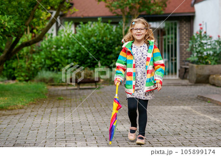 Little girl on way to elementary school or kindergarden. Preschool Child with colorful rainbow umbrella and waterproof jacket with school bag. Kid walking in autumn shower. Outdoor fun by any weather Little girl on way to elementary school or kindergarden. Preschool Child with colorful rainbow umbrella and waterproof jacket with school bag. Kid walking in autumn shower. Outdoor fun by any weather 105899174