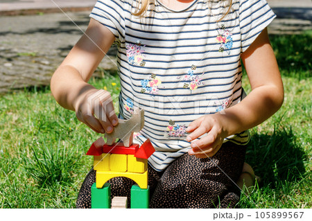 Little preschool girl playing with wooden blocks on the table outdoors. Educational game for small children. Happy child builds a tower from wooden rainbow stacking blocks. 105899567