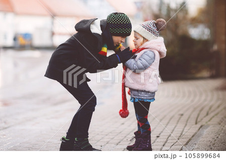 School kid boy and brother warming hands of little sister, toddler girl on cold snowy grey winter day. Family, two lovely siblings children playing with snow, outdoors during snowfall. School kid boy and brother warming hands of little sister, toddler girl on cold snowy grey winter day. Family, two lovely siblings children playing with snow, outdoors during snowfall. 105899684
