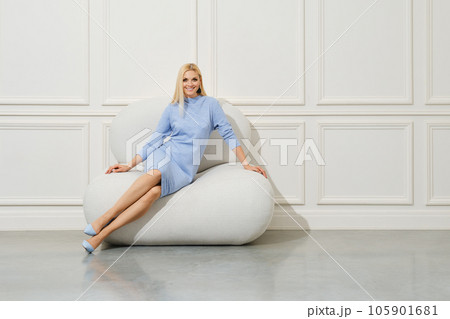 Joyful woman in knitted dress sitting on soft armchair 105901681