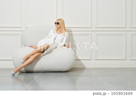 Sensual woman in total white outfit half laying on big soft chair Sensual woman in total white outfit half laying on big soft chair 105901689
