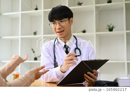 Smiling male general practitioner in white medical uniform giving consultation, explaining treatment to female patient Smiling male general practitioner in white medical uniform giving consultation, explaining treatment to female patient 105902217