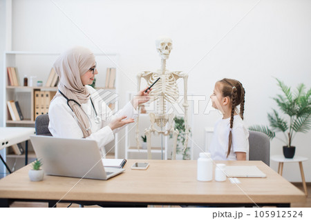 Physician consulting little girl using skeleton in hospital 105912524