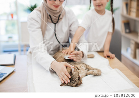 Woman in hijab observing cat while girl distracting animal 105912600