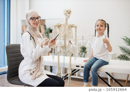 Female GP and tween girl posing near skeleton in exam room Female GP and tween girl posing near skeleton in exam room 105912664